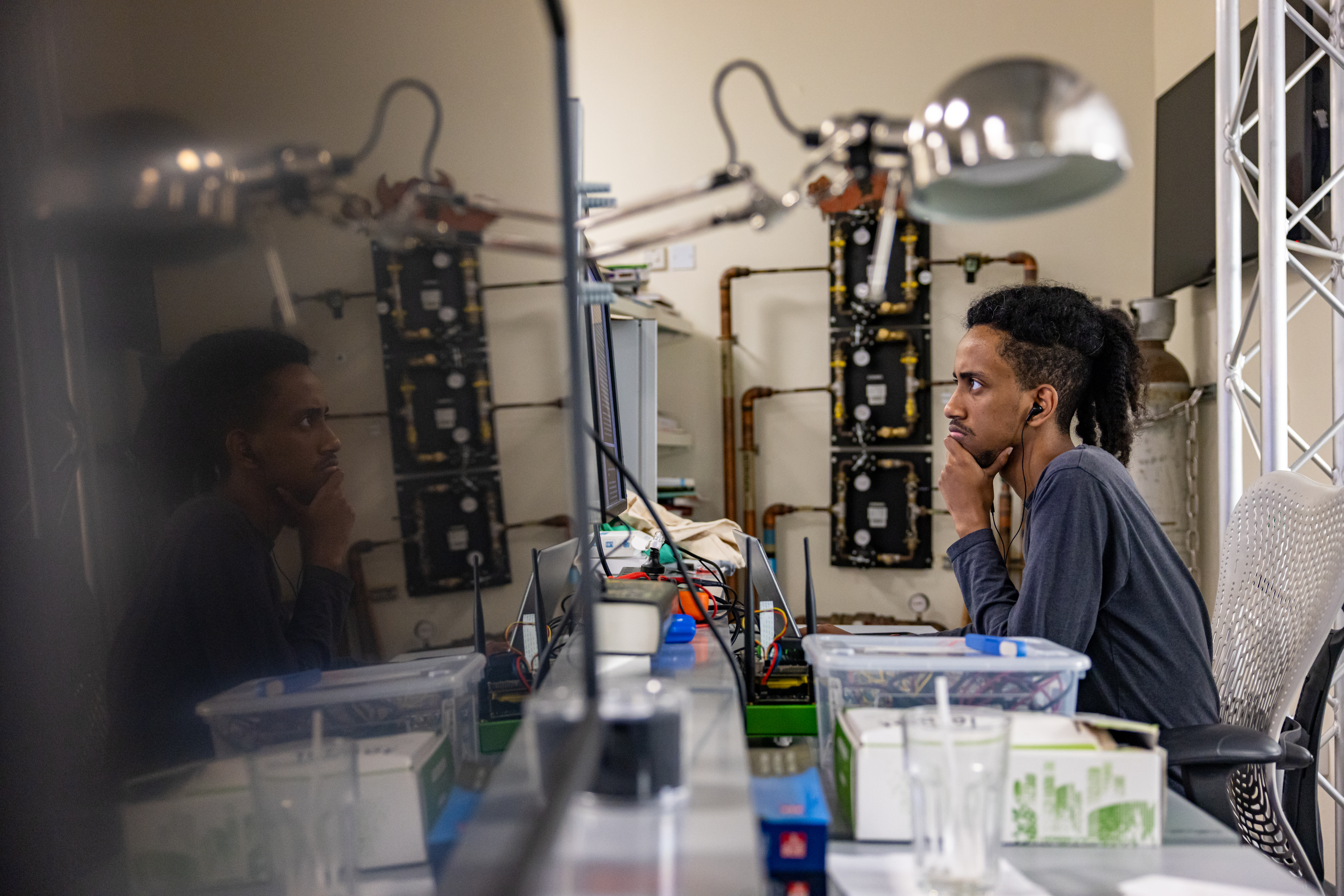 A student working in a lab, surrounded by computers and equipment.