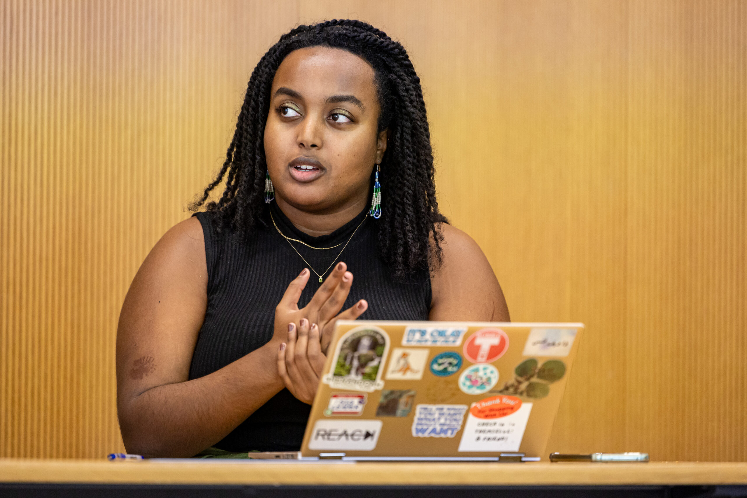 A student speaking in class with their laptop decorated with stickers in front of them.