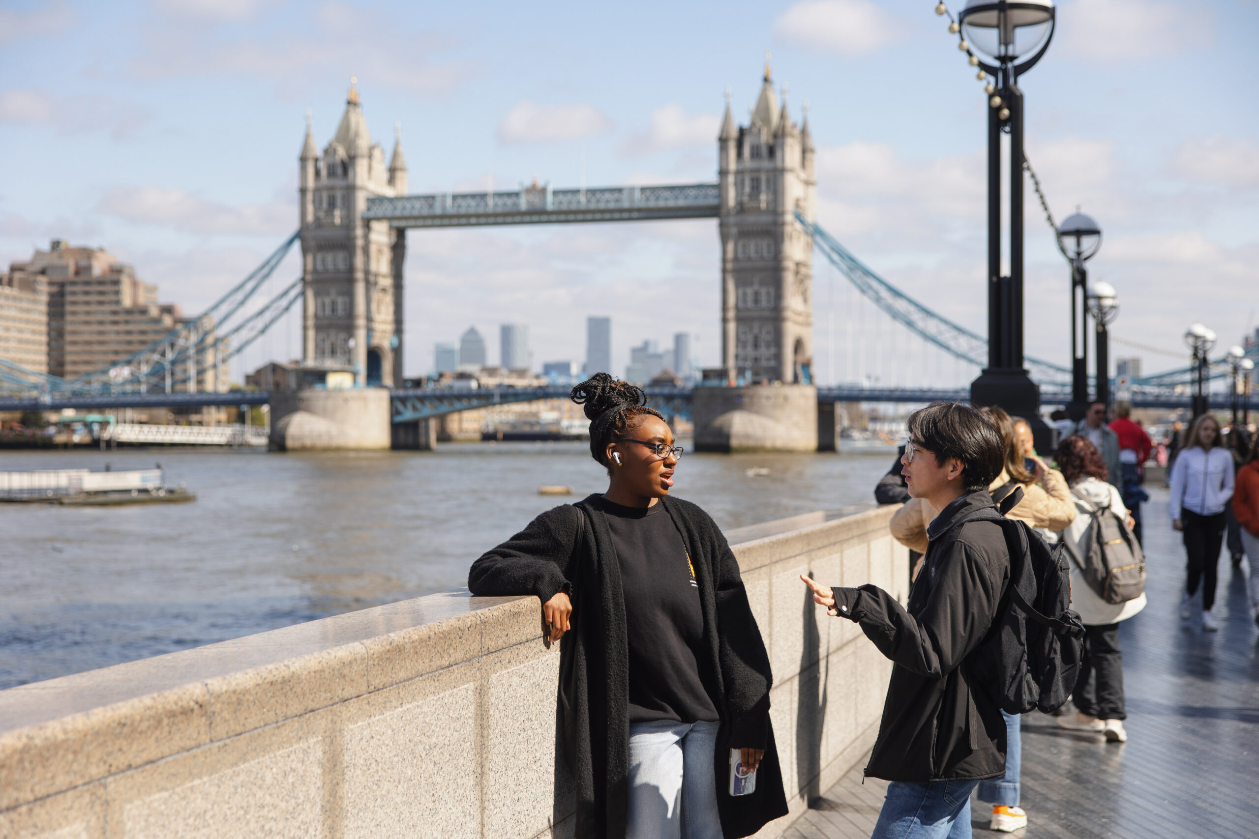 Two students out exploring London with the Thames River and Tower Bridge behind them