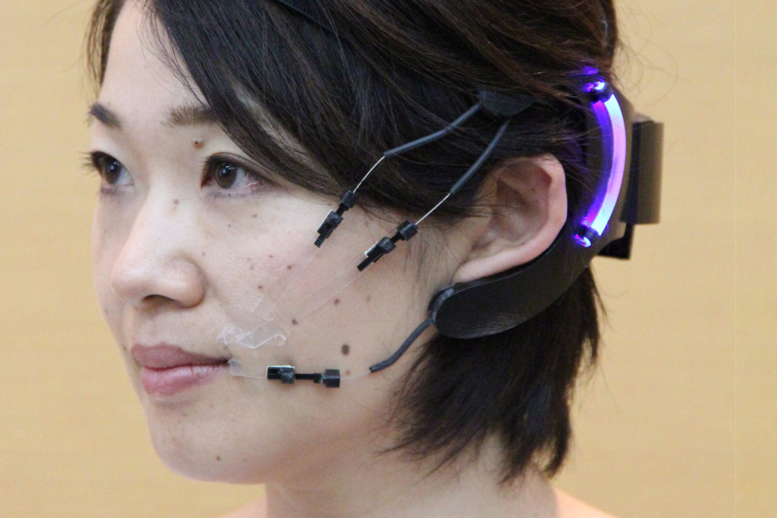 A student with an measuring equipment on their head along with small black dots on their face for recording purposes