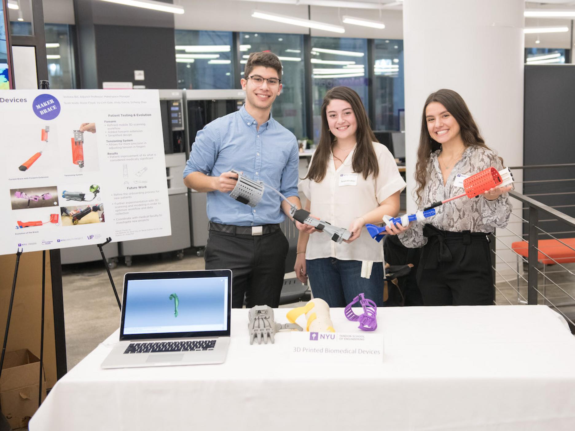 Three students holding up their engineering projects next to a poster board explaining their design